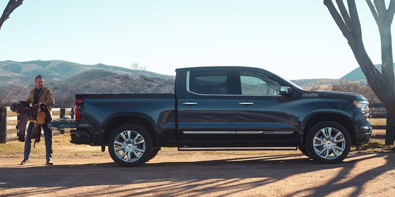 Black Chevrolet Silverado 1500 parked in a rural setting, with a man carrying a saddle near the truck