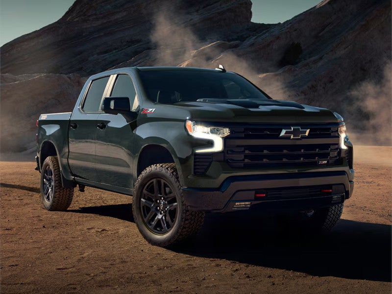 A rugged black pickup truck is parked on a dusty dirt path against a backdrop of rocky hills, conveying strength and adventure under a clear sky.